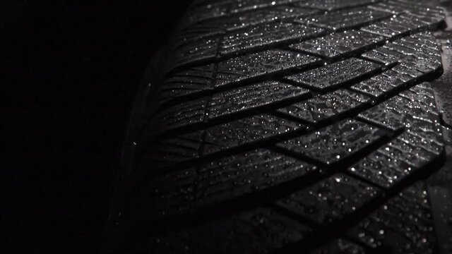Rotation of Wet Car Tire. The geometric pattern of the wheel in water droplets slowly rotates towards the viewer. Drops sparkle on the black rubber on a black background