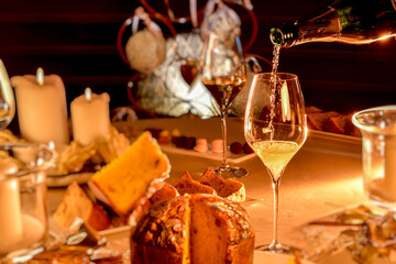 champagne is poured into glass on table set in Christmas style with  blurred panettone and candles,...