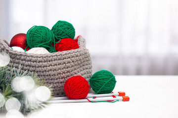 Green and red yarn in a knitted gray basket on a white table. Home comfort and christmas concept. Women's and men's hobby knitting.