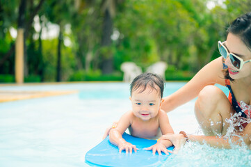 Asian mother and little son enjoying swimming in a swimming pool in summer vacation.