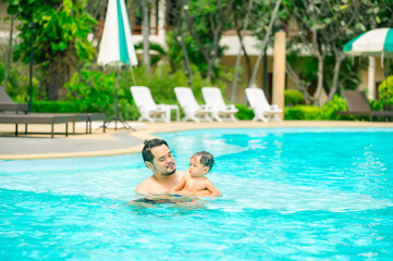 Asian father swimming with cute adorable baby in swimming pool.