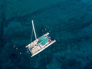 Aerial view of a catamaran with people on board and in the sea, swimming near the coasts of the island of Lanzarote, Canary, Spain. Jet ski performing in the sea
