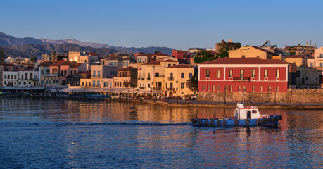 Fishing boat pass by Old Venetian harbour quay, Maritime museum of Crete in Chania, Crete, Greece. Sunrise, Cretan hills and mountains. First sun rays