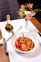 A dish of meat and a vase of flowers on a table..