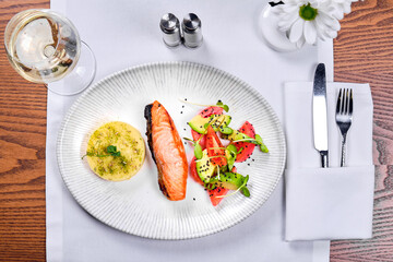 A dish of red fish and a glass of wine on a table in a restaurant.