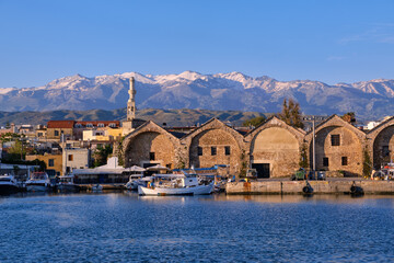 Fishing boats anchored by piers of Old Venetian shipyards or Neoria. Church bell tower and minaret, distant Cretan mountain. Chania, Crete, Greece. © NPershaj