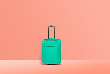 Turquoise suitcase standing, pink wall. Concept of tourism and traveling