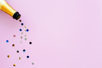 Champagne bottle with bright confetti on a pink background, flat lay. Creative holiday composition with copy space