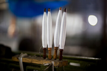 White yarn spools close-up in a yarn factory. White yarn spools in dark background.