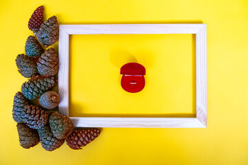 Wooden photo frame with cones and wedding ring on a yellow background
