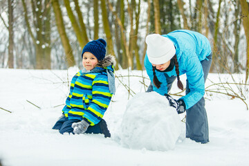 Fototapeta na wymiar mother with toddler son making snowman. rolling big snowball