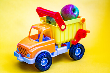 Toy truck on a yellow background with apples. Cargo transportation of fruit.