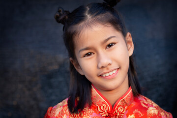 Cute little girl in Chinese dress smiles looking at the camera while standing in front of black background