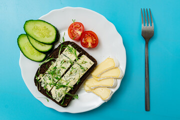 Rye bread with blue cheese and sprouted grains and tomatoes on a plate on a blue background.