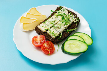 Rye bread with blue cheese and sprouted grains and tomatoes on a plate on a blue background.