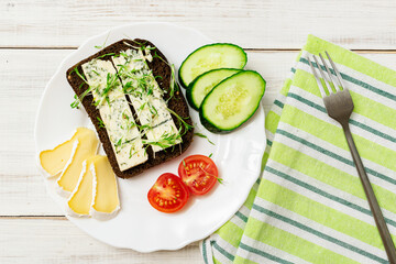 Blue cheese sandwich, brie cheese, cucumber and tomatoes on a plate on a wooden background. Healthy food.