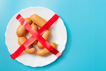 Refusal, prohibition to eat sausages, sausage. Crossed-out sausages on a plate on a blue background.