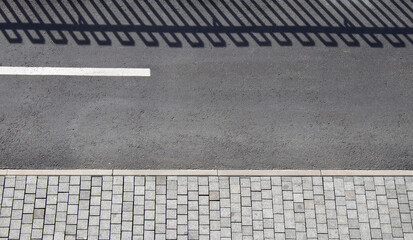 Fototapeta premium Detail of promenade road with bicycle lane, pedestrian sidewalk and shadow of a fence