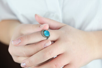 Fototapeta premium female hands trying on silver ring with blue and white gems. young woman wearing white blouse with well groomed hands. love, wedding and gift concept. 