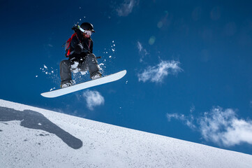 Young woman on a snowboard makes a flight after jumping from a snowy ledge against a dark blue sky...