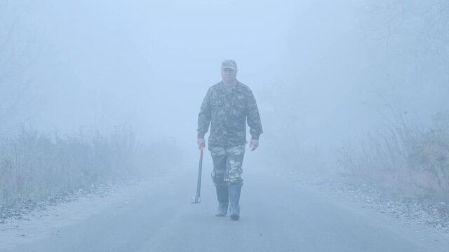 Strange man with an axe walks down the road in the fog.