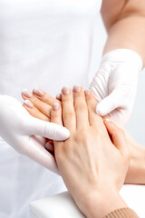 Fototapeta na wymiar Manicurist wearing gloves doing wax massage on female hands with manicure in nail salon