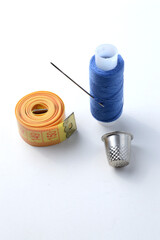 thimble, needle with thread and measuring tape on a white background .close-up.