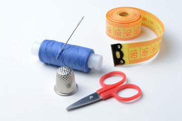 thimble, needle with spool of thread, scissors and measuring tape on a white background .close-up.