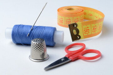 thimble, needle with spool of thread, scissors and measuring tape on a white background .close-up.