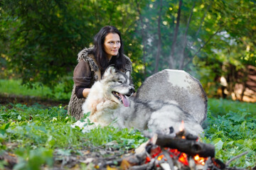 Shaman woman with an Alaskan Malamute next to the fire in the forest