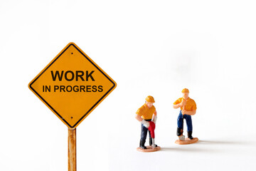 Small figure workers on white background with message Work In Progress 