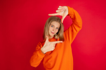 Framing face with hands. Portrait of young caucasian woman isolated on red studio background with copyspace. Beautiful female model. Concept of human emotions, facial expression, sales, ad, youth.
