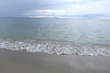 Obraz premium The waves on the beach hit the shore and the cloudy sky.