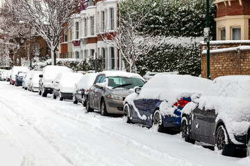 Street winter cityscape with snow terraced houses and frozen cars after a blizzard snowfall in London England UK, stock photo image with copy space