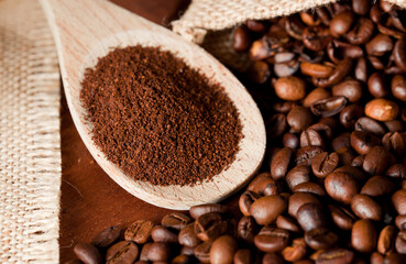coffee powder (ground), on wooden spoon, coffee beans, with raffia cloth bag, brown background
