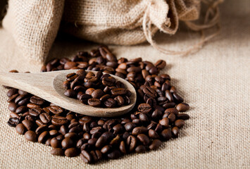Coffee, on wooden spoon, with raffia cloth bag, brown background