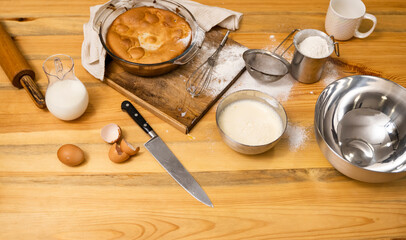 Tasty apple pie on a oaken wood table with a ingredients. Cooking a delicious apple pie on a kitchen in a loft style. Milk, eggs, sugar and a baked pie on a table. Home kitchen.