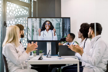 Fototapeta premium Video conference, telemedicine. Multiethnical medical scientific team applauding during a video conference with their female African colleague, expressing her excitement by clenching fists