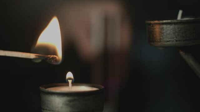 Close up of a match stick being lit by a woman and igniting multiple tealights in a silver candle holder in the background at night. Shot in 4K.