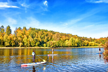 golden autumn landscape with people enjoying water sport activity on river against scenic blue sky...