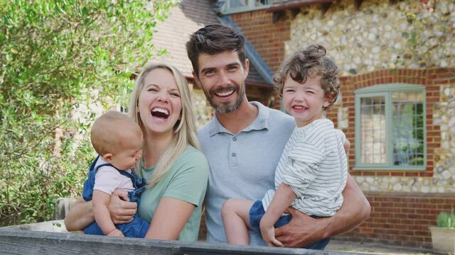 Loving family with baby girl standing outside house and smiling at camera - shot in slow motion