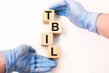 Word TBIL on wooden cubes held by hands in protective gloves on a white background with available space for copying. the medicine