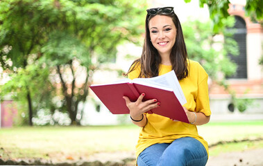 Beautiful female college student reading a book on a bench in a park