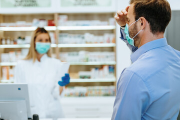 Customer with protective mask on his face buying pills in modern drugstore.