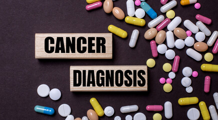 CANCER DIAGNOSIS is written on wooden blocks near multi-colored pills. Medical concept