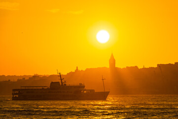 Fototapeta premium Galata Tower at sunset. Sun over the Galata Tower. Cityscape of Istanbul with Galata Tower at sunset. Galata Tower and a ferry