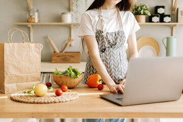 Young caucasian woman in apron use laptop computer in the modern kitchen, preparing salad, read recipe.