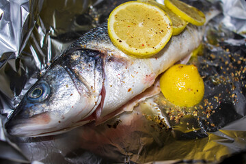 Fresh sea bass with lemon and spices on aluminum foil.