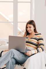 Attractive young caucasian woman use laptop computer, sitting on armchair in bright living room....