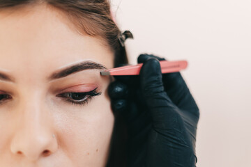 Eyebrow shaping procedure, make-up master uses tweezers to shape the eyebrows.